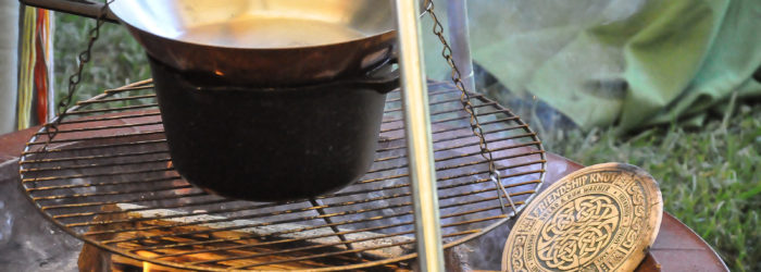 A pan in a pot on a hanging grill over a fire