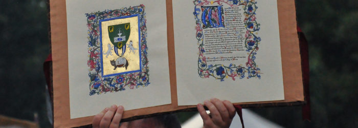 Person holding up a two-page award scroll with illuminated heraldry on the left and scroll text on the right